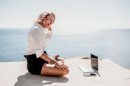 Happy girl doing yoga with laptop working at the beach. beautiful and calm business woman sitting with a laptop in a summer cafe in the lotus position meditating and relaxing. freelance girl remote work beach paradise