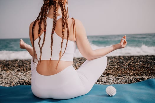 Woman yoga sea. Young woman with braids dreadlocks in white swimsuit and boho style braclets practicing outdoors on yoga mat by the ocean on sunny day. Women's yoga fitness routine. Healthy lifestyle, harmony