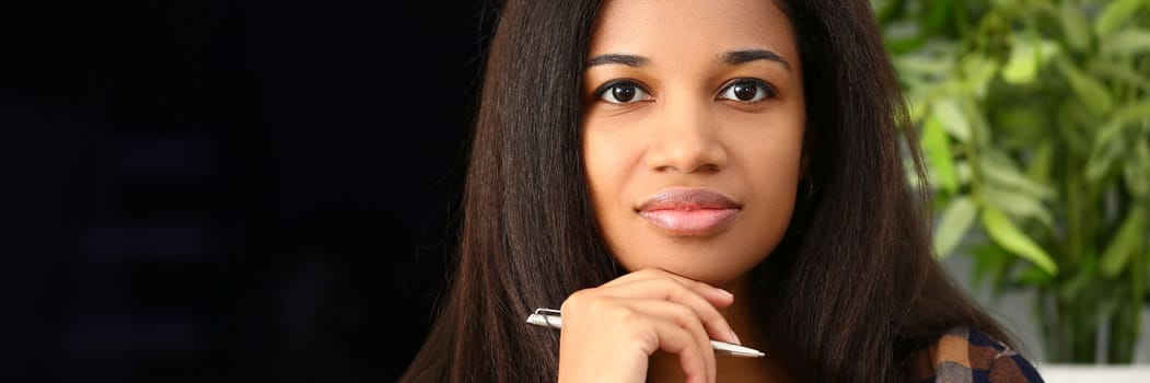 Thoughtful focused beautiful afro woman with pen. Portrait of smart dark-skinned young woman concept