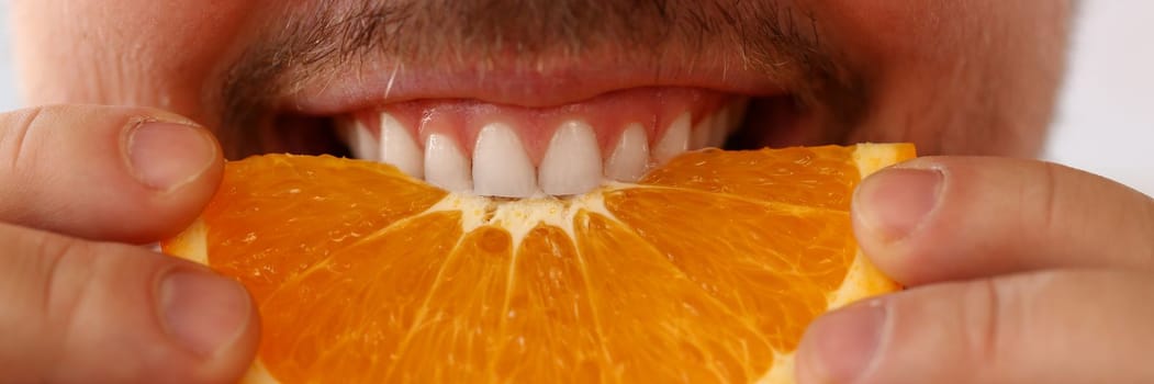 Bearded smiling man holds and bites orange fruit. Health benefits of oranges