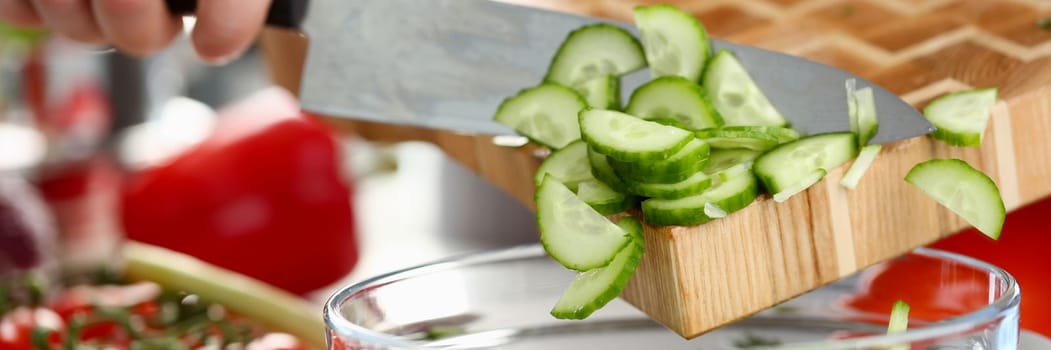 Preparing salad and sliced fresh cucumber at home. Cook throws cucumber from cutting board into salad and fresh vegetables