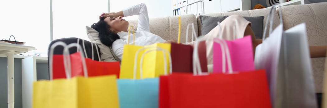 Tired woman sleeping on sofa with bags on floor. Shopping fatigue and stress