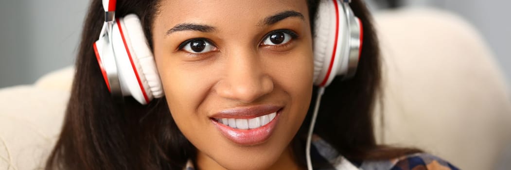 Smiling woman with headphones on sofa and listening to music. Application for watching movies or learning foreign languages