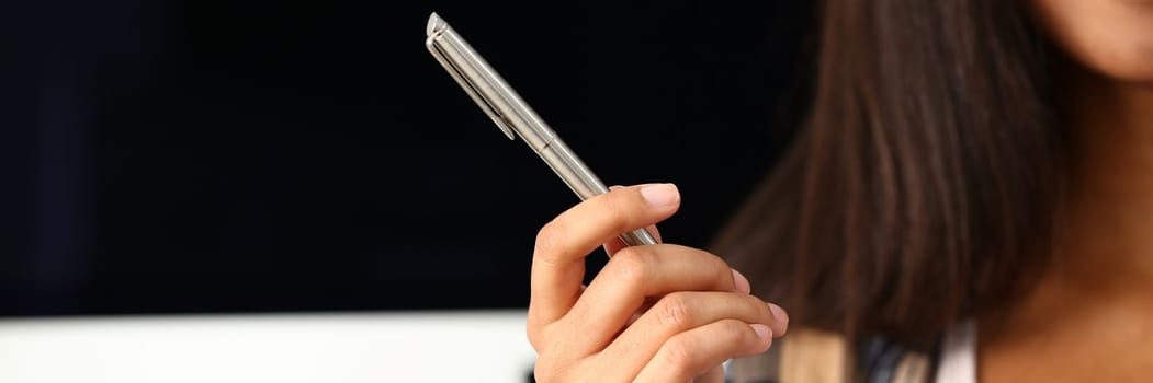 Woman hand holds metal pen on background of workplace. Gesture and sign training and education