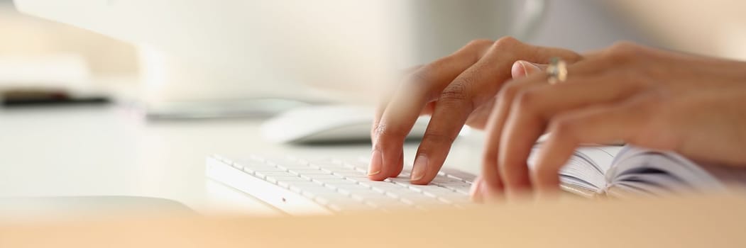 Closeup of female hands typing on keyboard and diary. Remote learning work and search for information on Internet