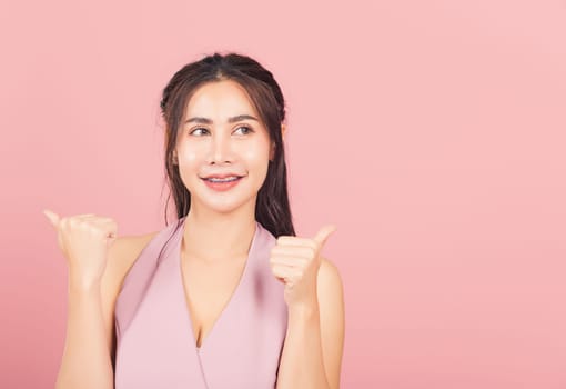 Portrait Asian beautiful young woman smile she standing made finger thumbs up, good sign to agree studio shot isolated on pink background, Thai female successful like finger gesture with copy space