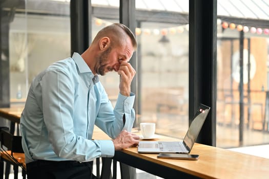 Tired caucasian businessman rubbing eyelids, feeling fatigue after long laptop use.