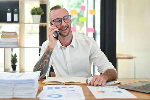 Handsome male financial advisor in eyeglasses answering or giving consultation to customer on mobile phone.