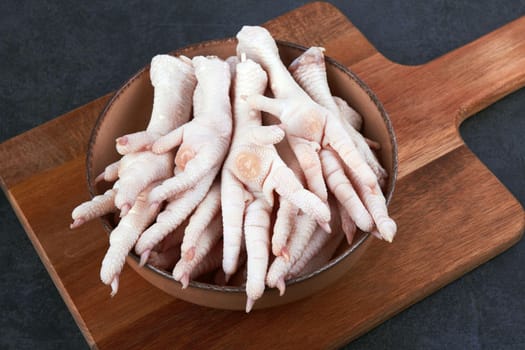 Raw chicken feet in bowl on black background