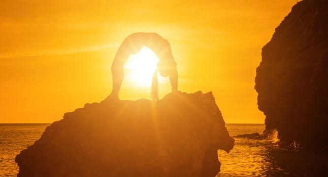 Young woman with black hair, fitness instructor in pink sports leggings and tops, doing pilates on yoga mat with magic pilates ring by the sea on the beach. Female fitness daily yoga concept