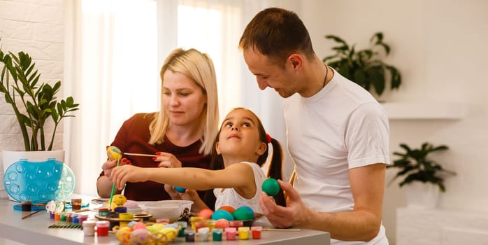 Happy family painting Easter eggs at table in kitchen