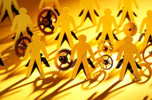 Lot of men figures cutting from yellow paper between gears