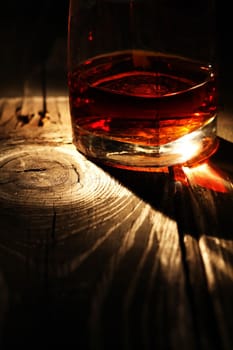 Still life with glass of whiskey against light on old wooden surface