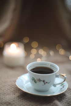 Details of still life in home interior of living room. Sweater, cup of tea, cotton, cozy, candle. Mug, candles and a garland bokeh on a dark cozy background. Decoration, vintage with glow bokeh