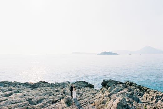 Bride and groom are standing on a rocky seashore overlooking the mountains. High quality photo
