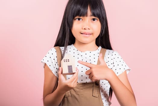 Asian little kid 10 years old hold wood house model on hands at studio shot isolated on pink background, Happy child girl with home model