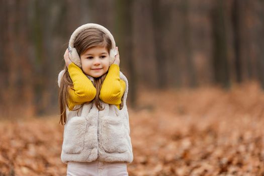 little girl in headphones walks through the autumn forest