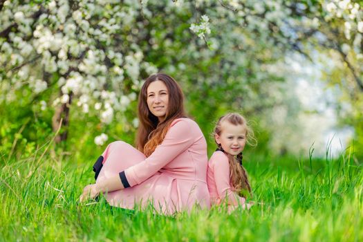 mother and daughter sit in a flowering garden with their backs to each other