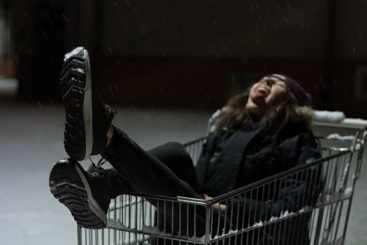 Happy young woman inside a shopping cart. Urban mood of a girl during a winter snow storm. High quality photo