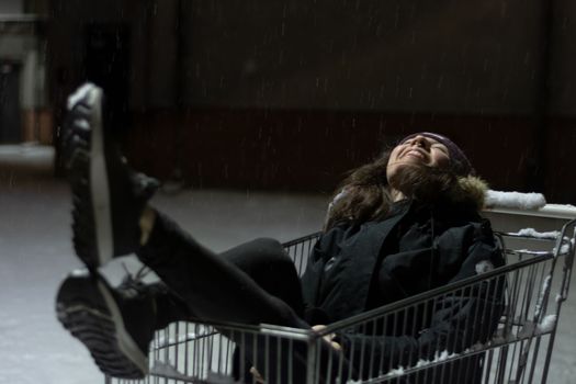 Happy young woman inside a shopping cart. Urban mood of a girl during a winter snow storm. High quality photo