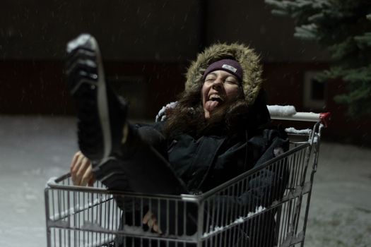 Happy young woman inside a shopping cart. Urban mood of a girl during a winter snow storm. High quality photo