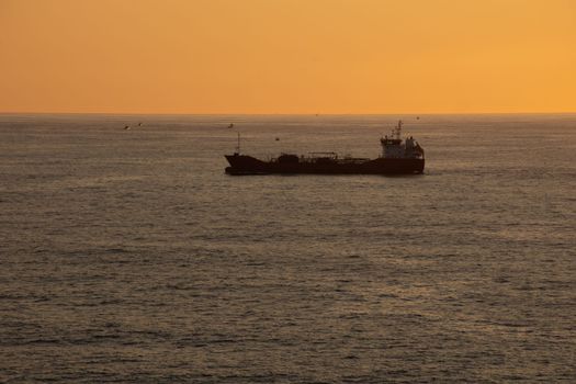 A trade cargo ship sailing alone at the sea in the Atlantic Ocean during sunset. High quality photo