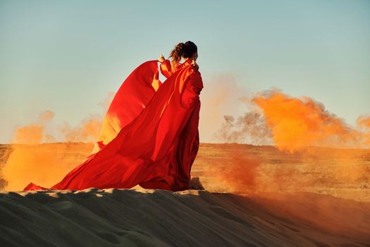 Woman in red dress dancing in the desert at blue sky