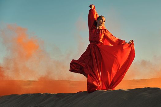 Woman in red dress dancing in the desert at blue sky