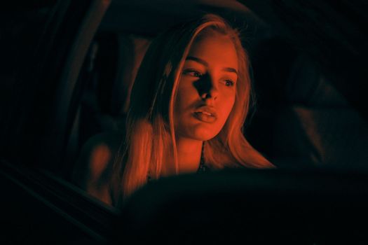 A beautiful girl of European appearance sits on the passenger seat in the car and looking to the window