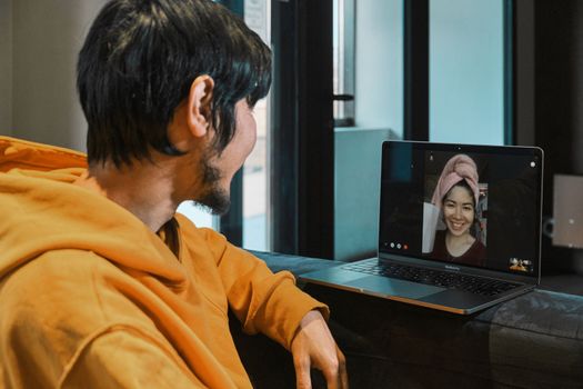 An Asian guy sits in a small office and communicates via video link through a laptop with his girlfriend. The concept of online communication, quarantine, distance.