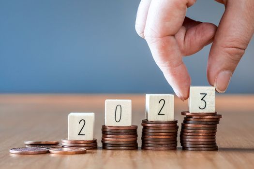 Hand place wooden cube 2023 on top stack of coins with sky blue background and copy space. saving money and financial plan concept for investment in new year 2023. close up