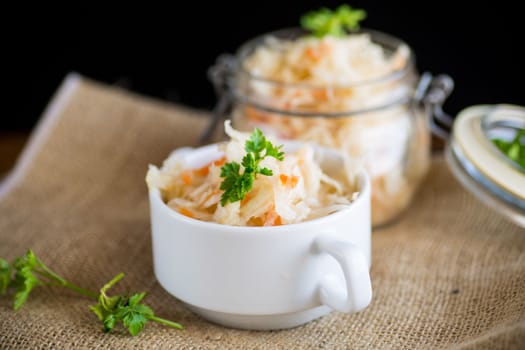 Sauerkraut with carrots and spices in a bowl on a wooden table.