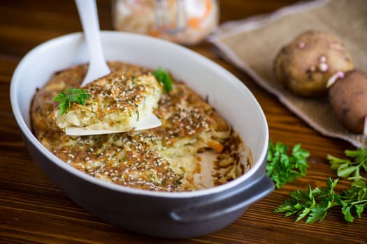 potato casserole with cabbage and spices in a ceramic form on a wooden table.