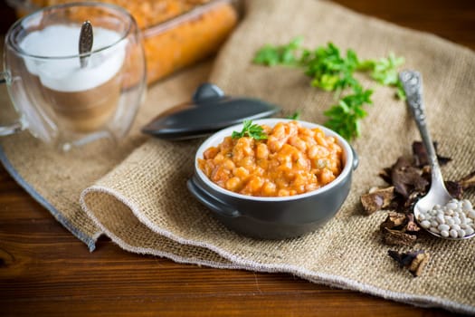 beans stewed with vegetables, mushrooms and spices, in a bowl, on a wooden table.