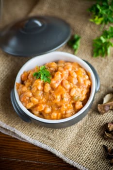 beans stewed with vegetables, mushrooms and spices, in a bowl, on a wooden table.