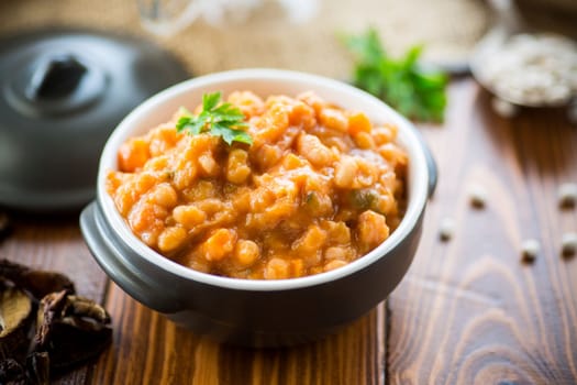 beans stewed with vegetables, mushrooms and spices, in a bowl, on a wooden table.