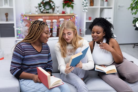 Girls read funny passages in the book and show them to each other. Christmas decoration. Smiling faces of female students.