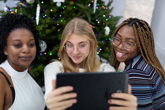 Christmas selfie of friends against the background of a Christmas tree. Funny photos taken with a tablet in a decorated living room at home.