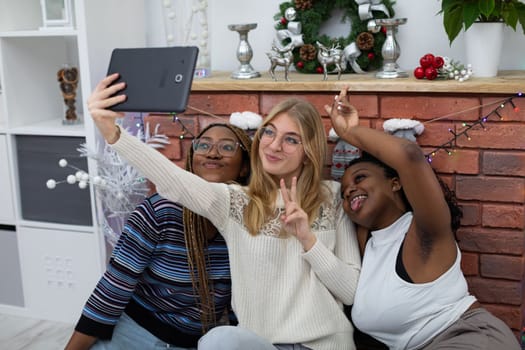 Friends take a selfie together by the decorated fireplace for Christmas. Friends from Africa and Europe.
