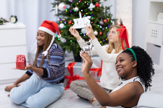 Happy African and European classmates experience Christmas together. Female students hold Christmas paraphernalia in their hands.