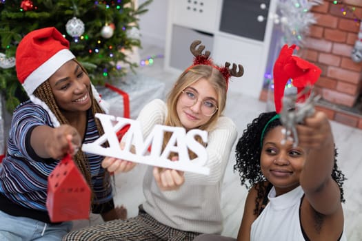Happily, the friends are spending Christmas together. A girl holds a Christmas sign in her hands. International Christmas of friends.