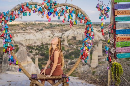 Young woman exploring valley with rock formations and fairy caves near Goreme in Cappadocia Turkey. Wish tree. Small multi-colored jugs with inscriptions, wishes hanging on the branches of a tree., against the backdrop of sand ruins and blue sky.