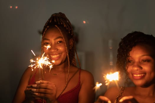 While celebrating the new year, two dark-skinned girls hold burning cold fires.