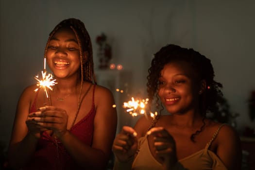 While celebrating the new year, two dark-skinned girls hold burning cold fires.