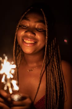 Cold fireworks during New Year's celebrations. A smiling dark-skinned woman holds a burning firework in her hand.
