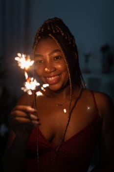 Cold fireworks during New Year's celebrations. A smiling dark-skinned woman holds a burning firework in her hand.