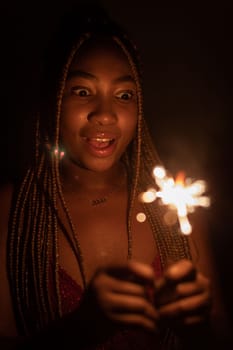 Cold fireworks during New Year's celebrations. A smiling dark-skinned woman holds a burning firework in her hand.