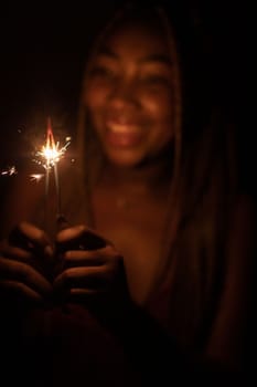 A girl with African beauty during the night of New Year's Eve lit cold fires and holds them in her hand. A happy and smiling student.