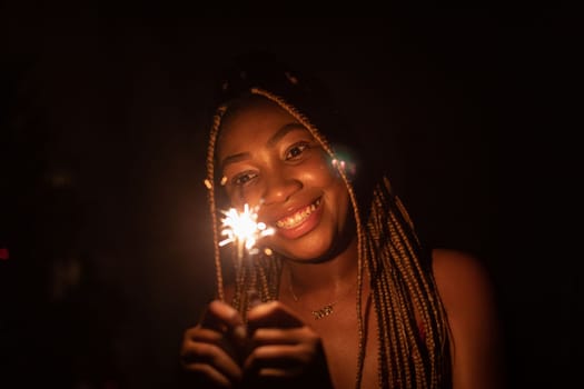 A girl with African beauty during the night of New Year's Eve lit cold fires and holds them in her hand. A happy and smiling student.