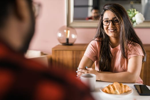 Young diverse loving couple eating croissant and talks together at home in breakfast time. Communication and relationship